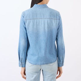 Model wearing LAgence blue denim shirt, back view, with long sleeves, curved hem, and button cuffs, styled with light blue jeans.
