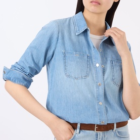 Model wearing LAgence blue chambray denim shirt with dual chest pockets and roll-tab sleeves, styled with a brown leather belt