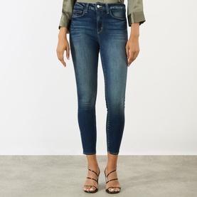 Model wearing L'Agence dark blue skinny jeans with raw hem detail, styled with a khaki top and strappy heeled sandals.