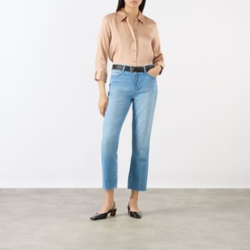 Model wearing LAgence light blue slim jeans with raw hem, styled with a beige shirt, black belt and black flat mules.