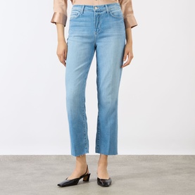Model wearing LAgence light blue slim jeans with raw hem cuffs, styled with a blush top and black mule heels.