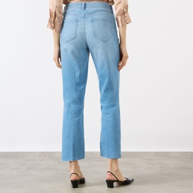 Model wearing LAgence light blue slim jeans, rear view, cropped ankle length, styled with black kitten heel mules and beige top.