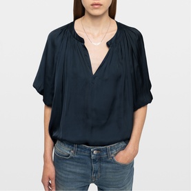 Model wearing Zadig blue relaxed V-neck blouse with gathered neckline and short sleeves, styled with light-wash jeans and delicate necklace.