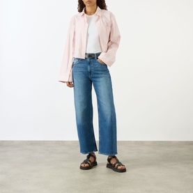 Model wearing Paige Arellia Ankle Wide-Leg Jeans in Stoneview, styled with a pink jacket, white tee and black sandals.