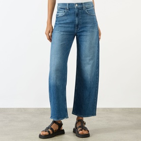 Model wearing Paige Arellia Ankle Wide-Leg Jeans in Stoneview. Mid-rise, wide-leg cut with frayed hems, styled with black chunky sandals.