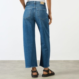 Model wearing Paige Arellia Ankle Wide-Leg Jeans in Stoneview, showing rear view with logo patch, distressed hem accents and wide-leg fit.