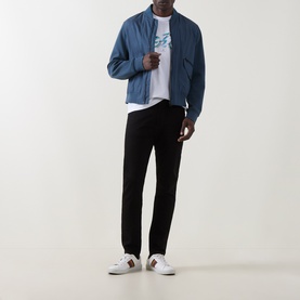 Model wearing Paul Smith Cycle Logo T-Shirt in white, styled with a blue zip-up jacket, black trousers, and white trainers.