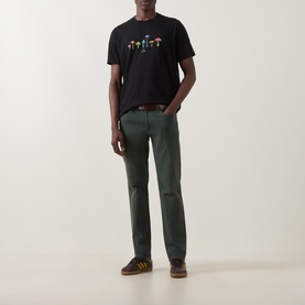 Model wearing Paul Smith Mushrooms Logo T-Shirt in black with colourful mushroom graphic, styled with dark green trousers and brown trainers.