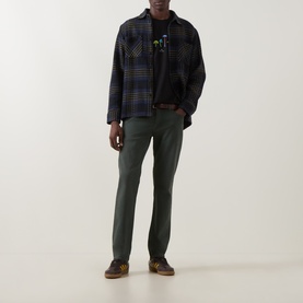 Model wearing Paul Smith Mushrooms Logo T-Shirt in black, styled with navy plaid overshirt, green trousers and brown shoes.