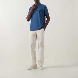 Model wearing Paul Smith Indigo Crew Neck T-Shirt with chest graphic, styled with cream wide-leg trousers and white trainers.