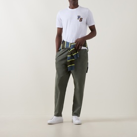 Model wearing Paul Smith white crew neck T-shirt with chest logo, styled with olive cargo trousers and striped shirt tied at waist.