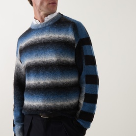 Model wearing Paul Smith Crew Neck jumper in black and blue graduated stripe, styled with white shirt and navy trousers.