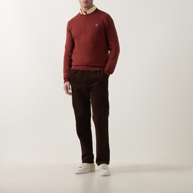 Model wearing Paul Smith Brick Red cotton crew neck sweater, styled with dark brown corduroy trousers and white trainers.