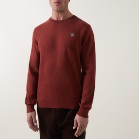 Model wearing Paul Smith Brick Red cotton crew neck jumper with embroidered zebra logo, styled with dark brown trousers.