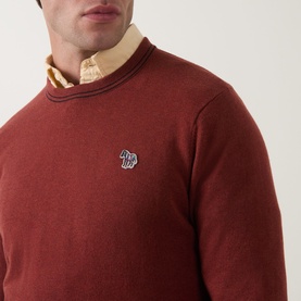 Model wearing Paul Smith Brick Red cotton crew neck jumper with zebra logo badge, styled over a yellow Oxford shirt collar visible at neckline.
