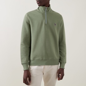 Model wearing Paul Smith Half Zip sweatshirt in light grey/green, with small zebra logo, quarter zip neckline, styled with cream trousers.