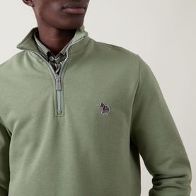 Model wearing Paul Smith Half Zip sweatshirt in light grey-green with zebra logo badge, layered over a checked shirt.