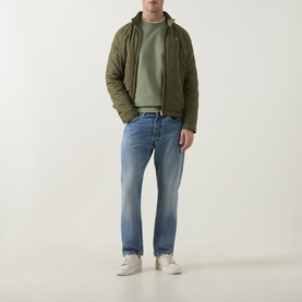 Model wearing olive quilted hooded jacket, sage green T-shirt, light wash straight jeans, and white trainers