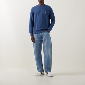 Model wearing Paul Smith Indigo cotton sweatshirt with Zebra logo patch, styled with light-wash wide-leg jeans and white trainers.