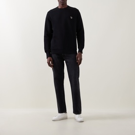 Model wearing Paul Smith black cotton sweatshirt with small chest logo, styled with dark jeans and white trainers.