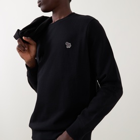 Model wearing Paul Smith black cotton sweatshirt with embroidered zebra logo badge, styled with a black jacket draped over shoulder.