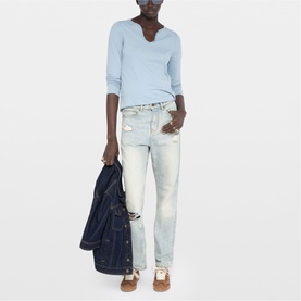 Model wearing Zadig blue long-sleeve top with notch neckline, styled with light-wash distressed jeans, holding a denim jacket.