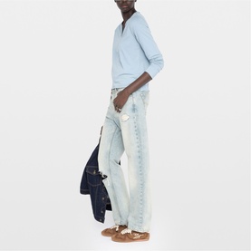 Model wearing Zadig blue long-sleeve top and light wash straight-leg jeans, carrying a dark denim jacket, with tan sandals.