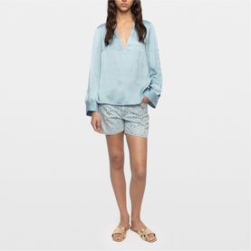 Model wearing Zadig blue relaxed V-neck blouse with long sleeves, styled with patterned shorts and flat gold sandals.