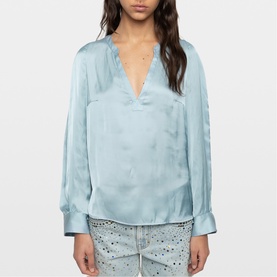 Model wearing Zadig blue satin blouse with deep V-neck, long sleeves and cuffed wrists, styled with embellished jeans.