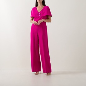 Model wearing Sisters fuchsia jumpsuit with flutter sleeves, V-neckline, wide-leg trousers and embellished waist detail, styled with strappy heels.