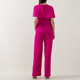 Model wearing Sisters fuchsia jumpsuit with cape overlay detail, shown from the back, wide-leg silhouette, short sleeves