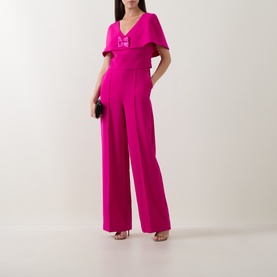 Model wearing Sisters fuchsia jumpsuit with flutter sleeves, wide-leg trousers and embellished bodice, styled with strappy heels and clutch bag.