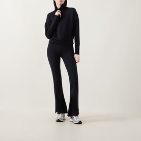 Model wearing Spanx AirEssentials&reg; Track Jacket in Very Black with matching flared trousers and grey trainers.