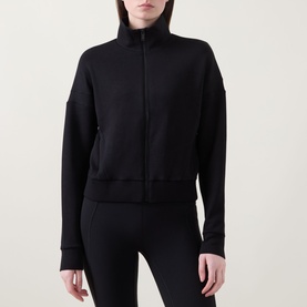 Model wearing Spanx AirEssentials&reg; Track Jacket in Very Black with mock neck, zip fastening and ribbed cuffs, styled with black leggings.