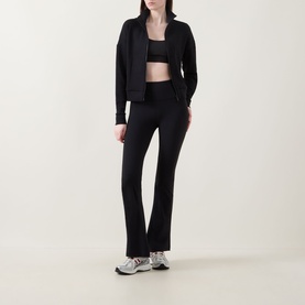 Model wearing Spanx AirEssentials&reg; Track Jacket in Very Black with matching flared trousers, black sports bra and white trainers.