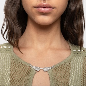 Model with silver wing-shaped statement necklace, styled with green open-knit top