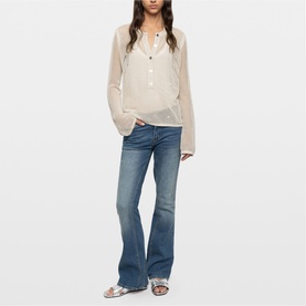 Model wearing Zadig beige semi-sheer button-front top with flared jeans and silver sandals