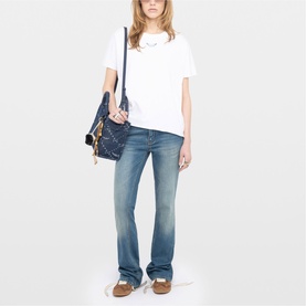 Model wearing Zadig white short-sleeve T-shirt with blue bootcut jeans, styled with a navy quilted shoulder bag and tan loafers