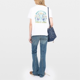 Model wearing Zadig white graphic print T-shirt with blue flare jeans, shown from behind, styled with a navy blue crossbody bag.
