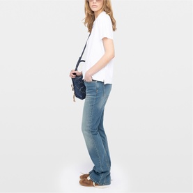 Model wearing Zadig white top with blue flared jeans, carrying a small dark navy crossbody bag, styled with tan loafers.