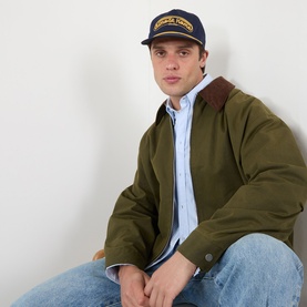 Model with Almost Home AH Studio Logo Baseball Cap in navy, styled with olive jacket and blue striped shirt