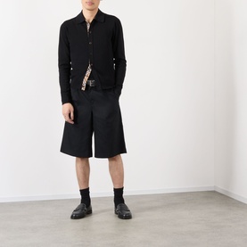 Model wearing black long-sleeve shirt and wide-leg black shorts, styled with a leopard-print scarf, black belt, socks and loafers