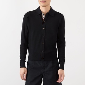 Model wearing black button-through knit polo shirt with collar, styled with printed shirt underneath and dark trousers