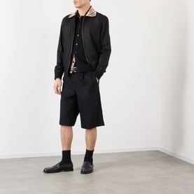 Model wearing black bomber jacket with check collar, styled with matching black shorts, black socks and black leather shoes