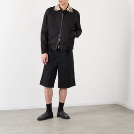 Model wearing Burberry Glenfields Harrington Jacket in black with check collar, styled with black shorts, socks and leather loafers.