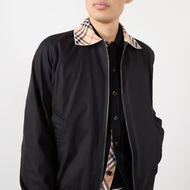 Model wearing Burberry Glenfields Harrington Jacket in black with signature check collar, shown open over dark shirt. Cotton construction.