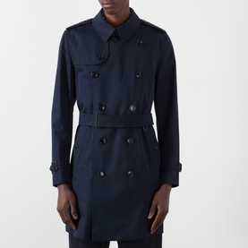 Model wearing Burberry Kensington Heritage Trench Coat in coal blue, double-breasted with epaulettes, belted waist and tabbed cuffs.