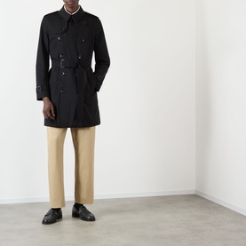 Model wearing Burberry Kensington Heritage Trench Coat in black, double-breasted with belt and epaulettes, styled with beige trousers and black shoes.