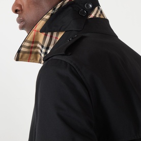 Model wearing Burberry Kensington Heritage Trench Coat in black, showing iconic check lining at collar and structured shoulder detail.
