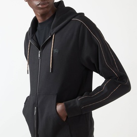 Model wearing Burberry Scott Embroidered Logo Zip Hoodie in black with contrast piping detail, hands in kangaroo pocket.
